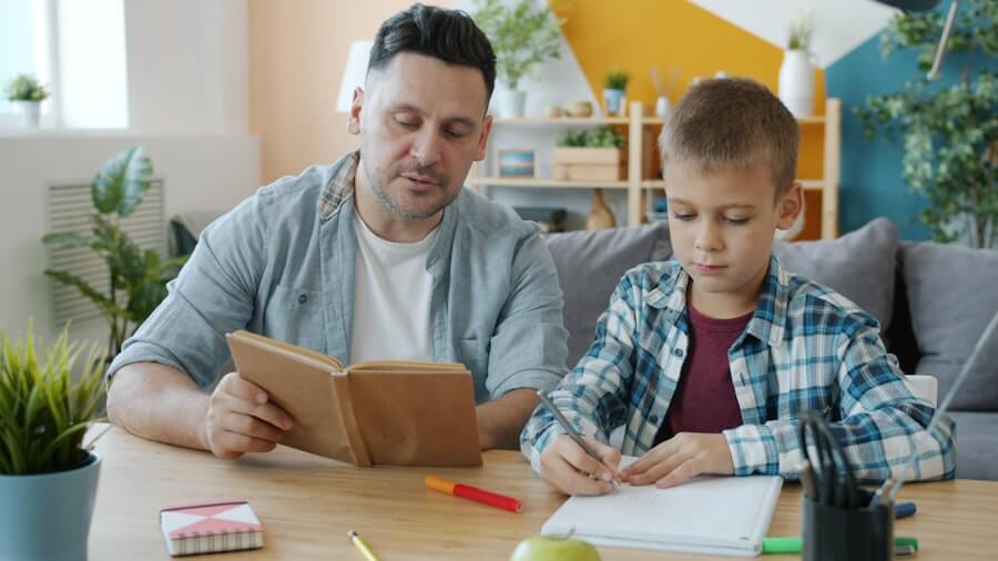 A parent and child sit together at a table, reading and writing.